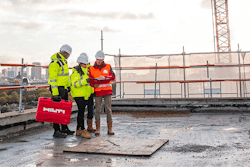 Three construction workers standing on a roof looking at plans.