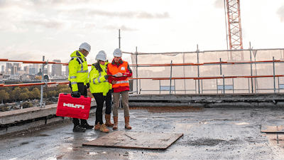 Three construction workers standing on a roof looking at plans.