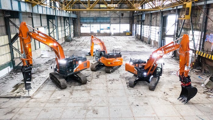 Three Hitachi excavators parked inside an industrial building