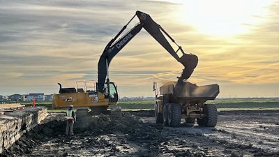 excavator dumping scoop of dirt into dump truck body