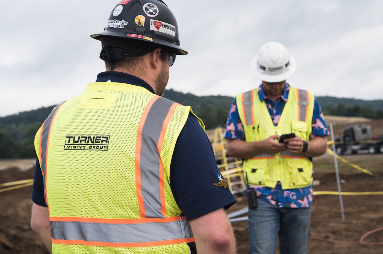 Miner wearing a hard hat and hi-vis vest texts on his cell phone