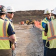 Four miners wearing hard hats and hi-vis vests at a mine site.