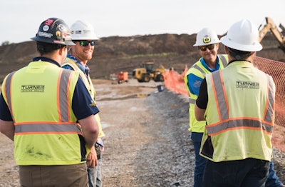 Four miners wearing hard hats and hi-vis vests at a mine site.