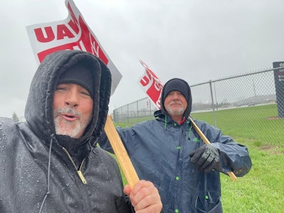 Two workers holding UAW on Strike signs and standing in a picket line outside a CNH Industrial plant