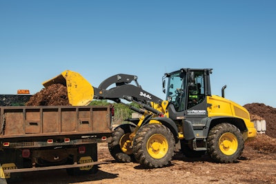 John Deere 344L compact wheel loader dumping mulch from bucket into dump truck bed