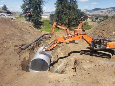 Excavators setting pipe in a trench.