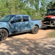 Light Blue 2022 Ford Maverick towing ATV on trailer on dirt road