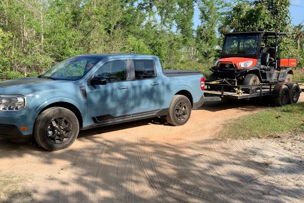 Light Blue 2022 Ford Maverick towing ATV on trailer on dirt road