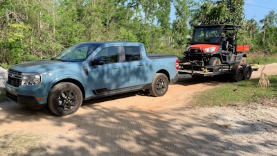 Light Blue 2022 Ford Maverick towing ATV on trailer on dirt road