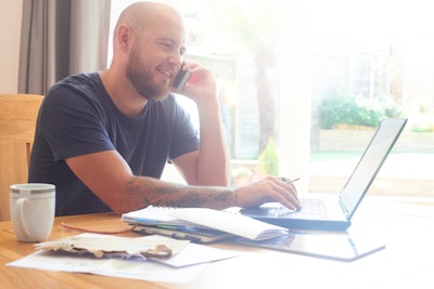 Man sitting at a table using a cell phone and laptop