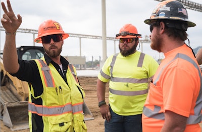 Construction workers talking next to a compact track loader