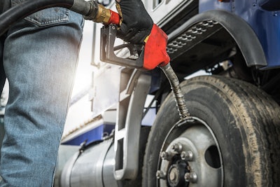 Person holding a fuel nozzle next to a semi-truck