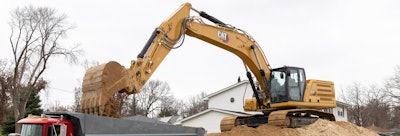 Cat 336 excavator dumping bucket load into dump truck from position atop dirt pile.