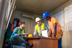 Construction workers wearing safety vests and hats inside a trailer on a jobsite