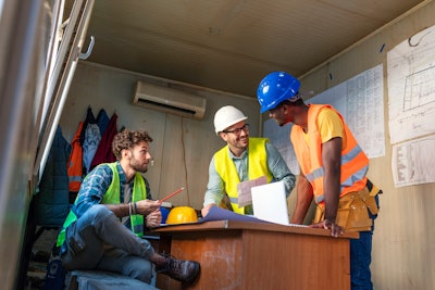 Construction workers wearing safety vests and hats inside a trailer on a jobsite
