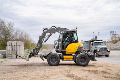 Mecalac 11MWR wheeled excavator carrying concrete block on pallet forks
