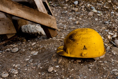 dirty yellow hard hat on dirt rocky ground beside wooden pallet