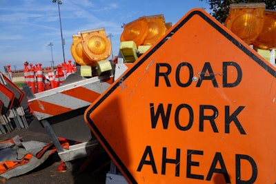 orange road work ahead sign with orange cones reflector lights in background