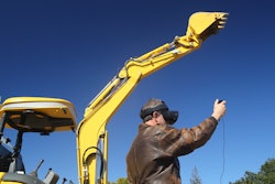 SRI International robot excavator operator with virtual reality goggles raises arm and excavator raises arm