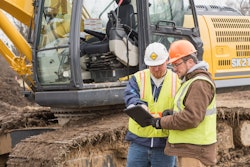 Two workers looking at tablet next to excavator