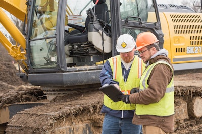 Two workers looking at tablet next to excavator