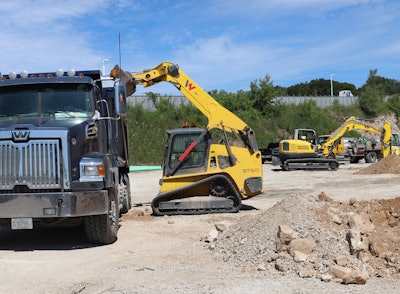 Wacker Neuson ST50 compact track loader with arms extended up bucket dumping into haul truck bed