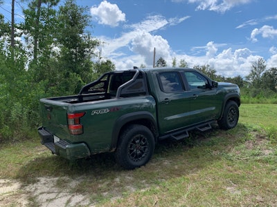 2022 Nissan Frontier Pro-4X pickup truck tactical green color side view parked on grassy hill with trees in background