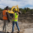 Male and female construction workers talking on jobsite excavators in background