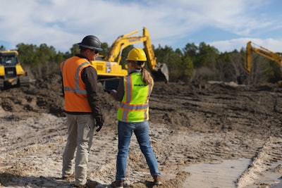 Male and female construction workers talking on jobsite excavators in background