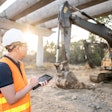 Construction worker with tablet looking at excavator