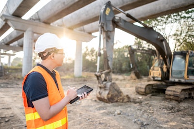 Construction worker with tablet looking at excavator