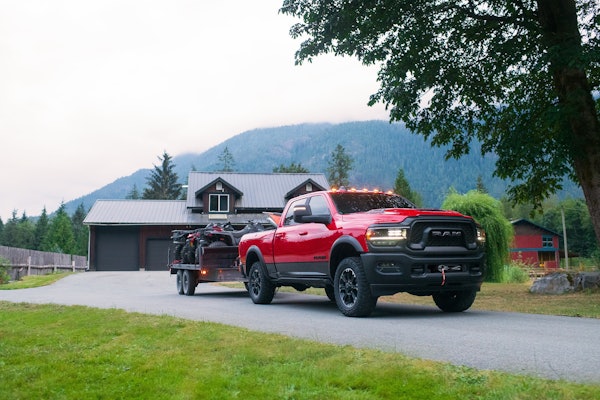 red 2023 Ram 2500 Rebel diesel towing ATVs with home and mountains in background
