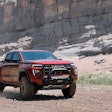 red 2023 GMC Canyon AT4X driving in desert beneath rock cliff