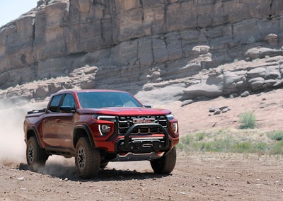 red 2023 GMC Canyon AT4X driving in desert beneath rock cliff