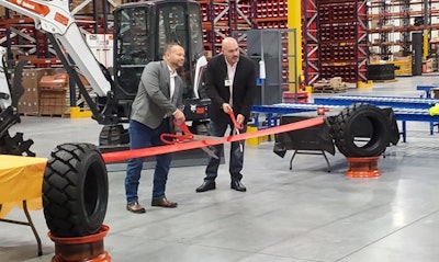 Two Bobcat executives cut red ribbon with big scissors on floor of new aftermarket parts warehouse