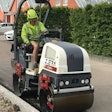 Dynapac CC900 e Z.ERA electric tandem-drum vibratory compactor with operator in high-vis green hardhat and vest compacting asphalt