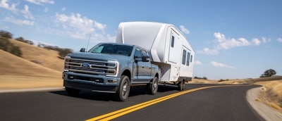 2023 Ford Super F-350 Limited blue-gray pickup truck pulling white camper on desert highway