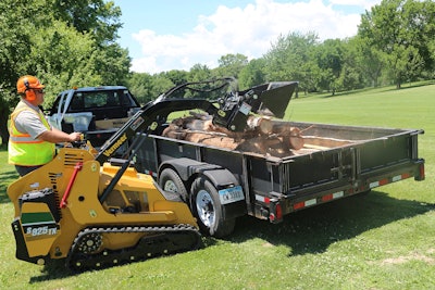 Vermeer S925TX -compact utility loader dumping logs in back of trailer in pasture