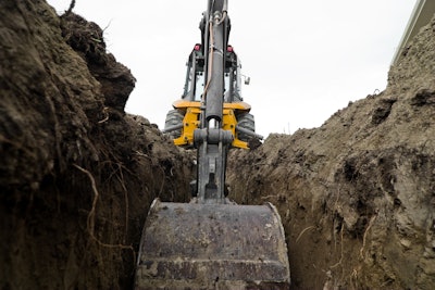 Backhoe digging trench in dirt stock image