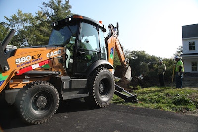 Case 580 EV electric backhoe backed up to yard