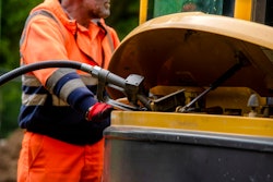 stock image worker in orange outfit pumping diesel into construction equipment tank