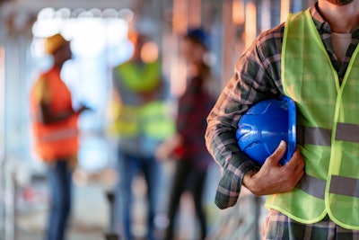 stock image construction worker wearing yellow vest carrying blue hard hat