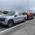 Ford F-150 Lightning towing Kubota tractor parked in parking lot