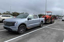 Ford F-150 Lightning towing Kubota tractor parked in parking lot
