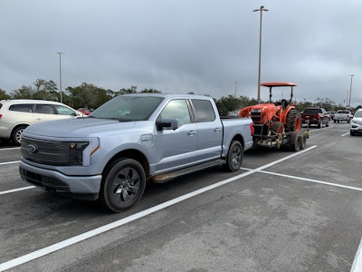 Ford F-150 Lightning towing Kubota tractor parked in parking lot