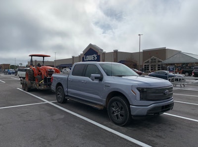 Ford F-150 Lightning with trailer hauling Kubota tractor in Lowe's parking lot
