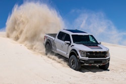 Stock 2023 Ford F-150 Raptor R pickup truck in avalanche gray shoots up sand behind it driving down dune