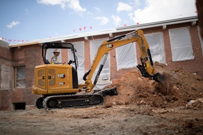 Cat 304 compact excavator digging in dirt beside building under construction