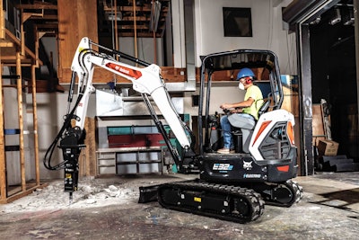 Bobcat E32e electric compact excavator breaking concrete floor inside building with hydraulic hammer attachment