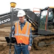 Worker in orange vest white hard uses Trimble Siteworks in front of Volvo excavator